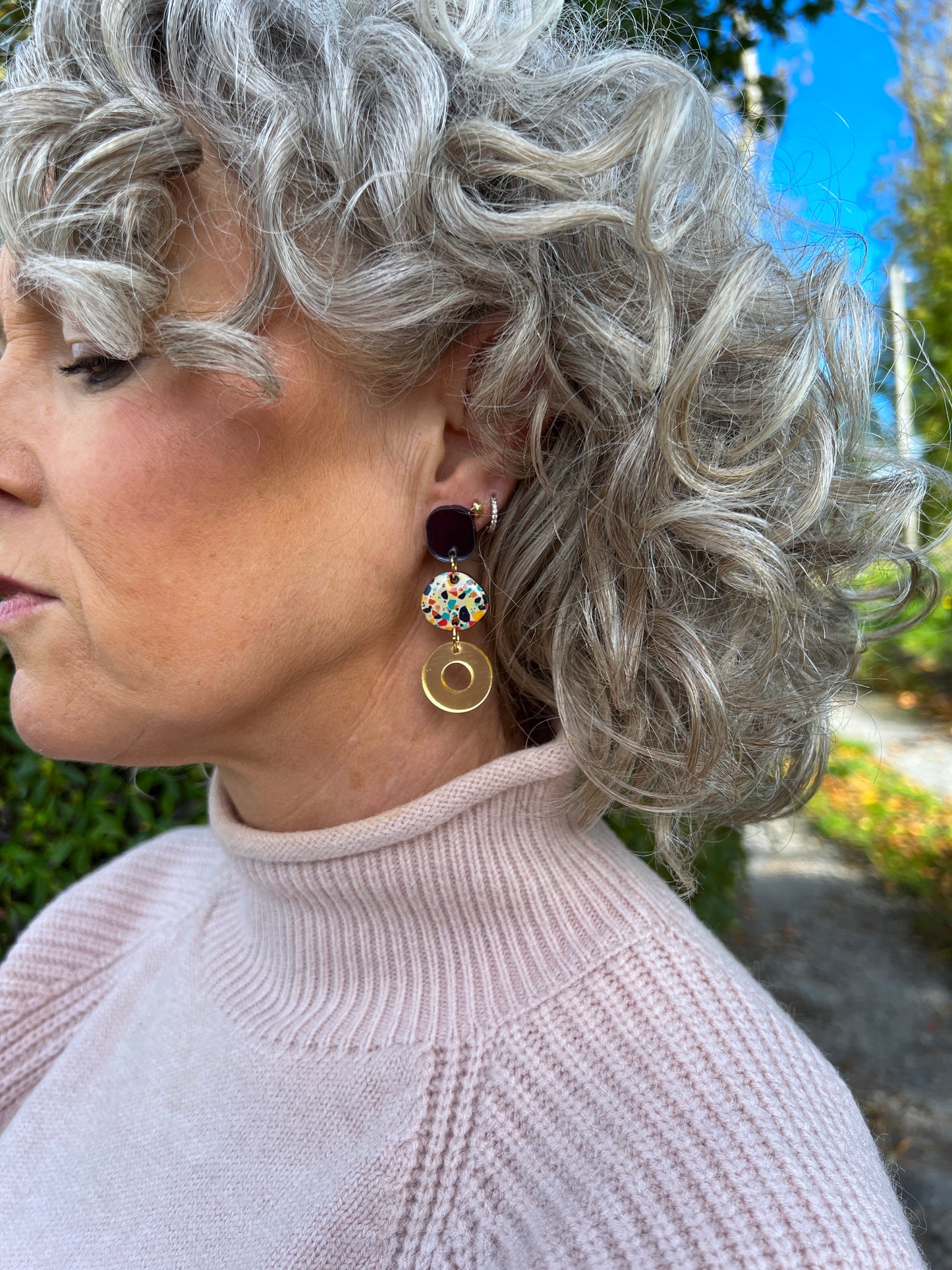 Woman with styled gray hair wearing colourful drop earrings outdoors