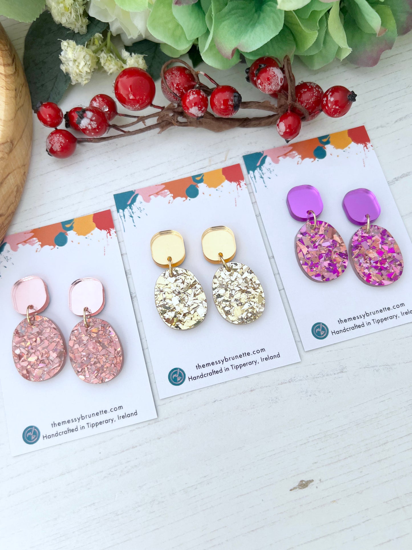 Three pairs of glitter earrings in rose gold, lavander in gold glitter on cards with a decorative background