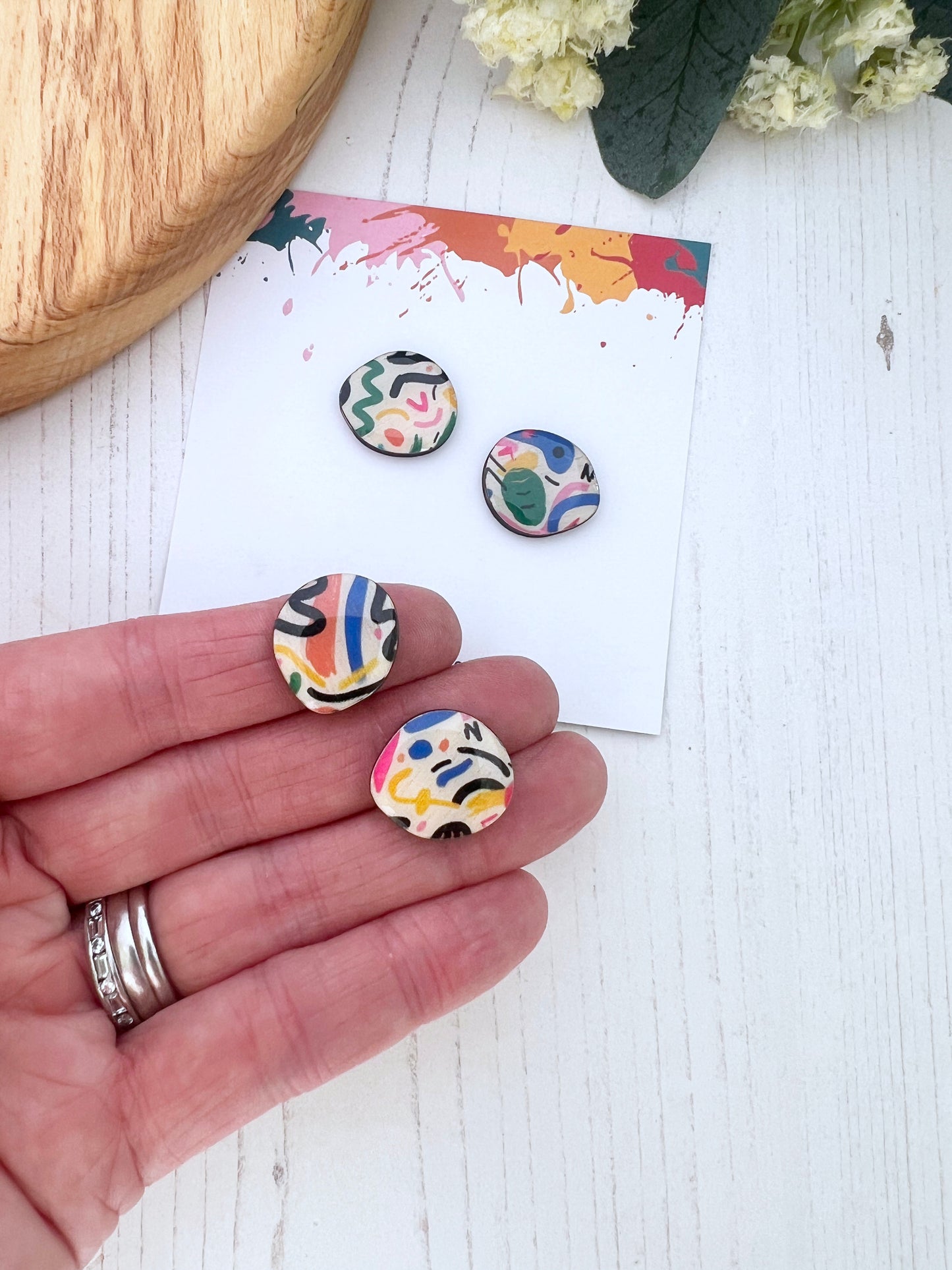 Colourful patterned earrings held in a hand with a white background