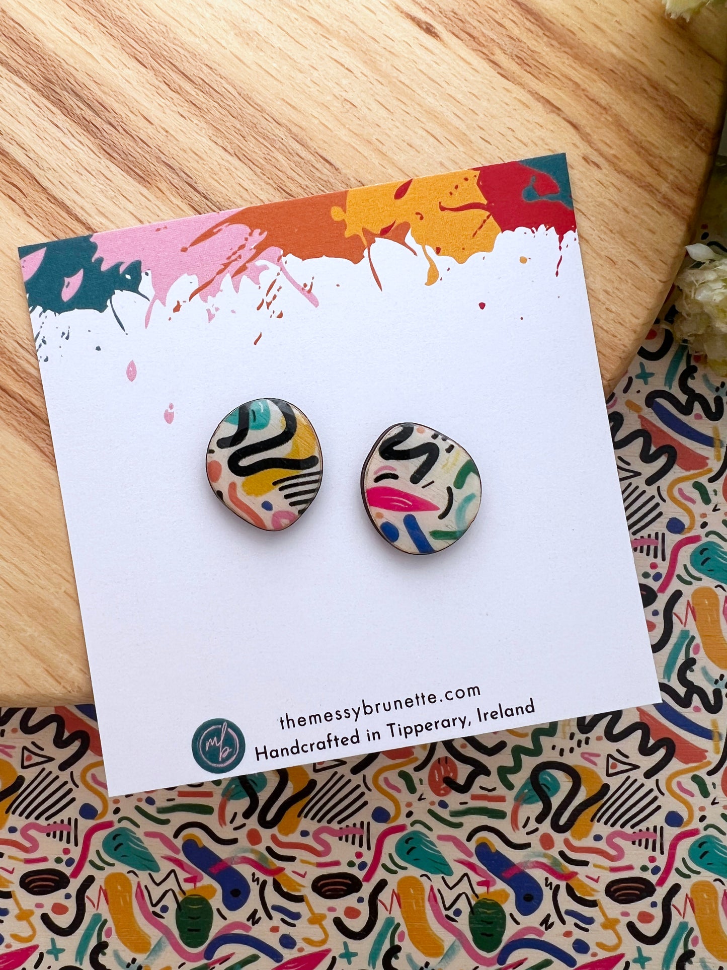 Pair of colourful abstract doodle wood stud earrings on a branded card with a patterned background.