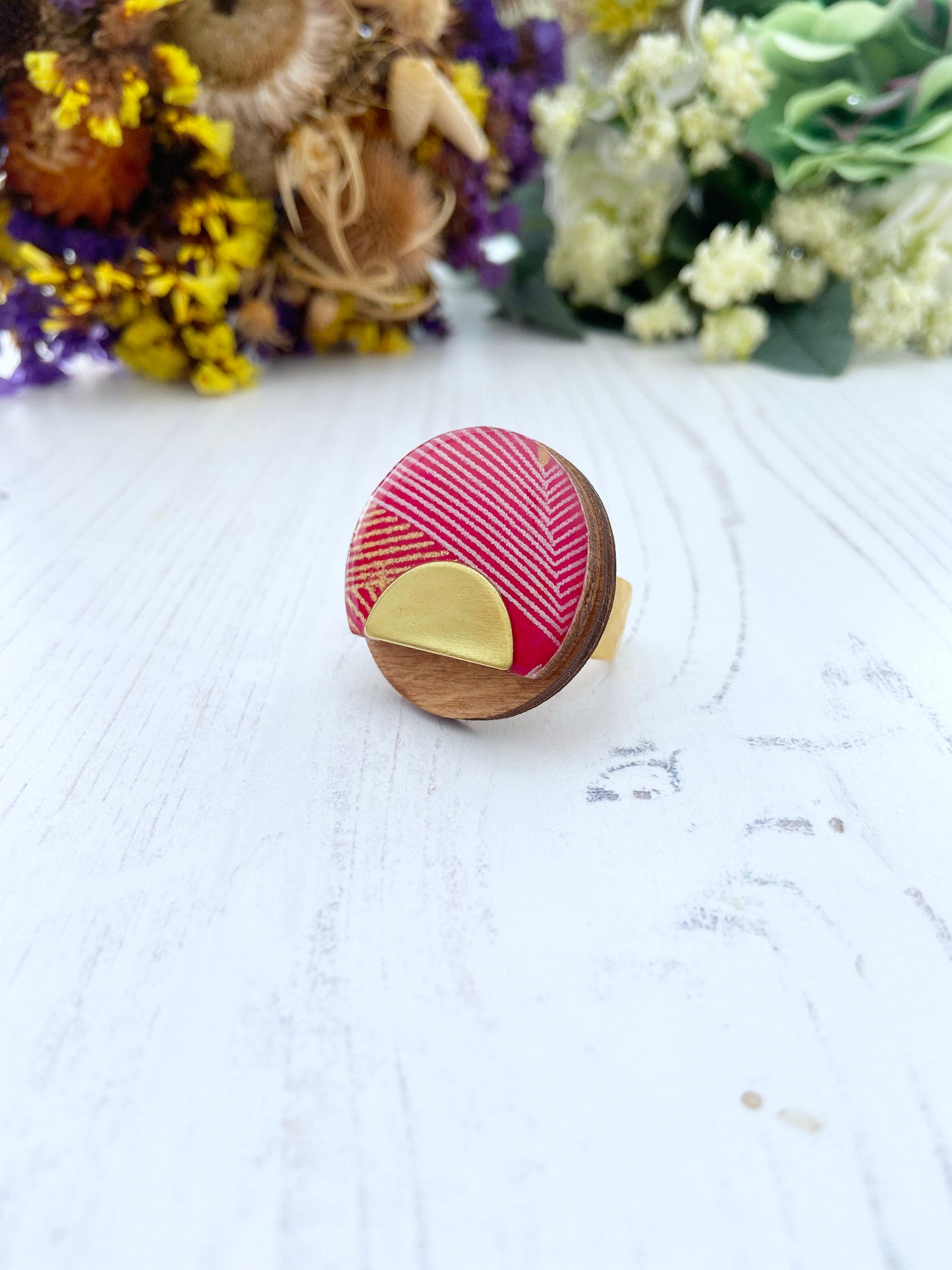 Wooden ring with red and gold design on a white surface with dried flowers in the background