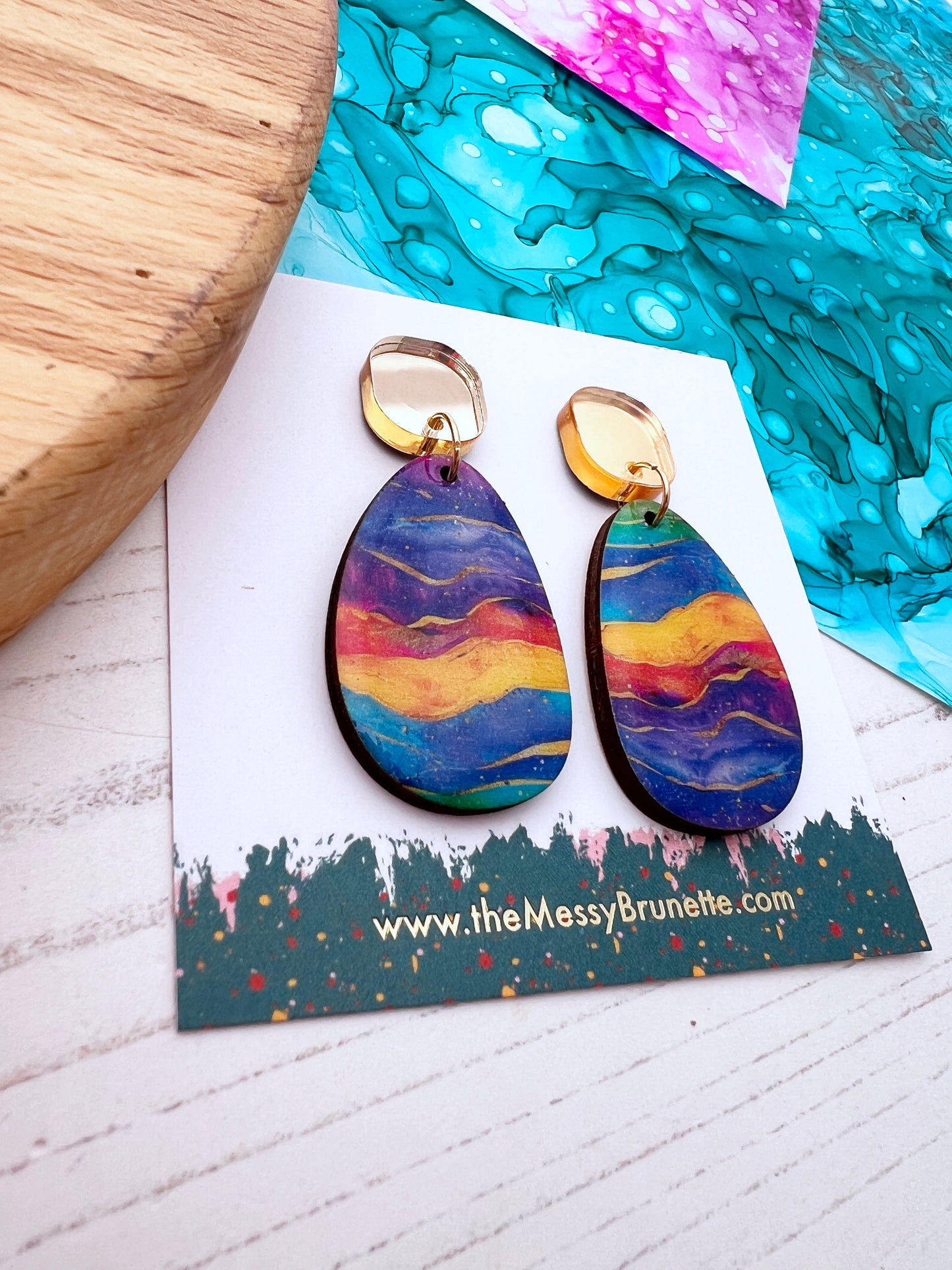 Multi coloured wood earrings on a branded card with a colourful background