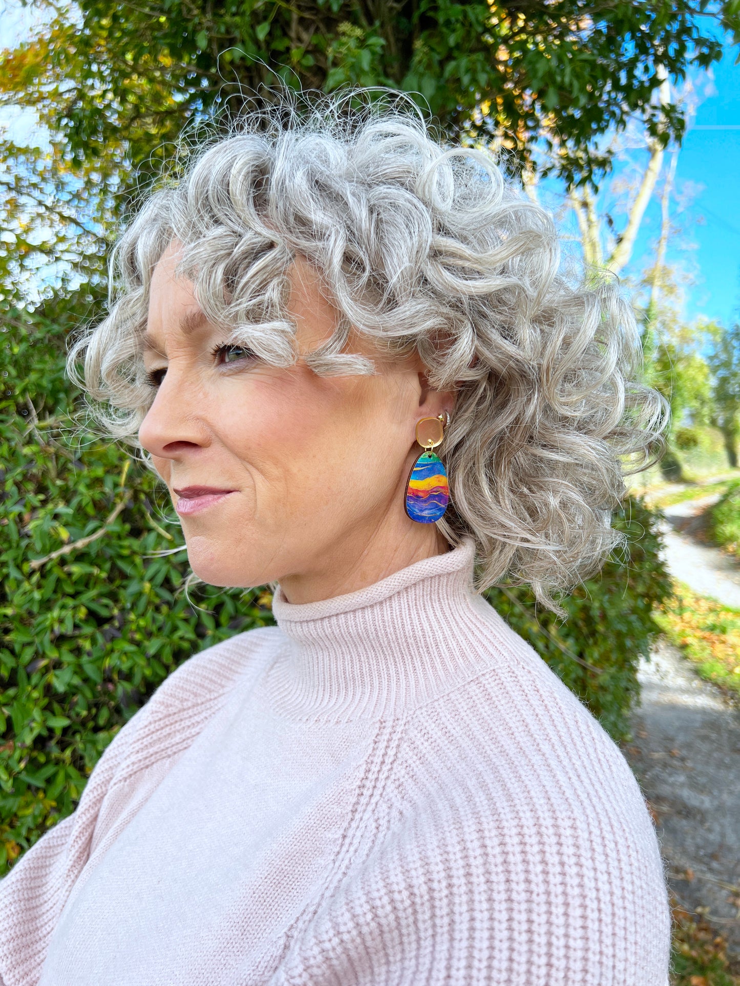 Person with gray hair wearing colourful earrings outdoors