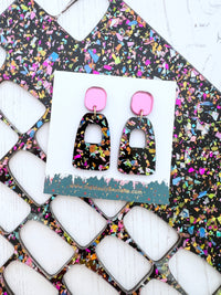 Pair of glitter shards patterned earrings with pink accents on a branded The Messy Brunette card, placed on a colourful abstract background.