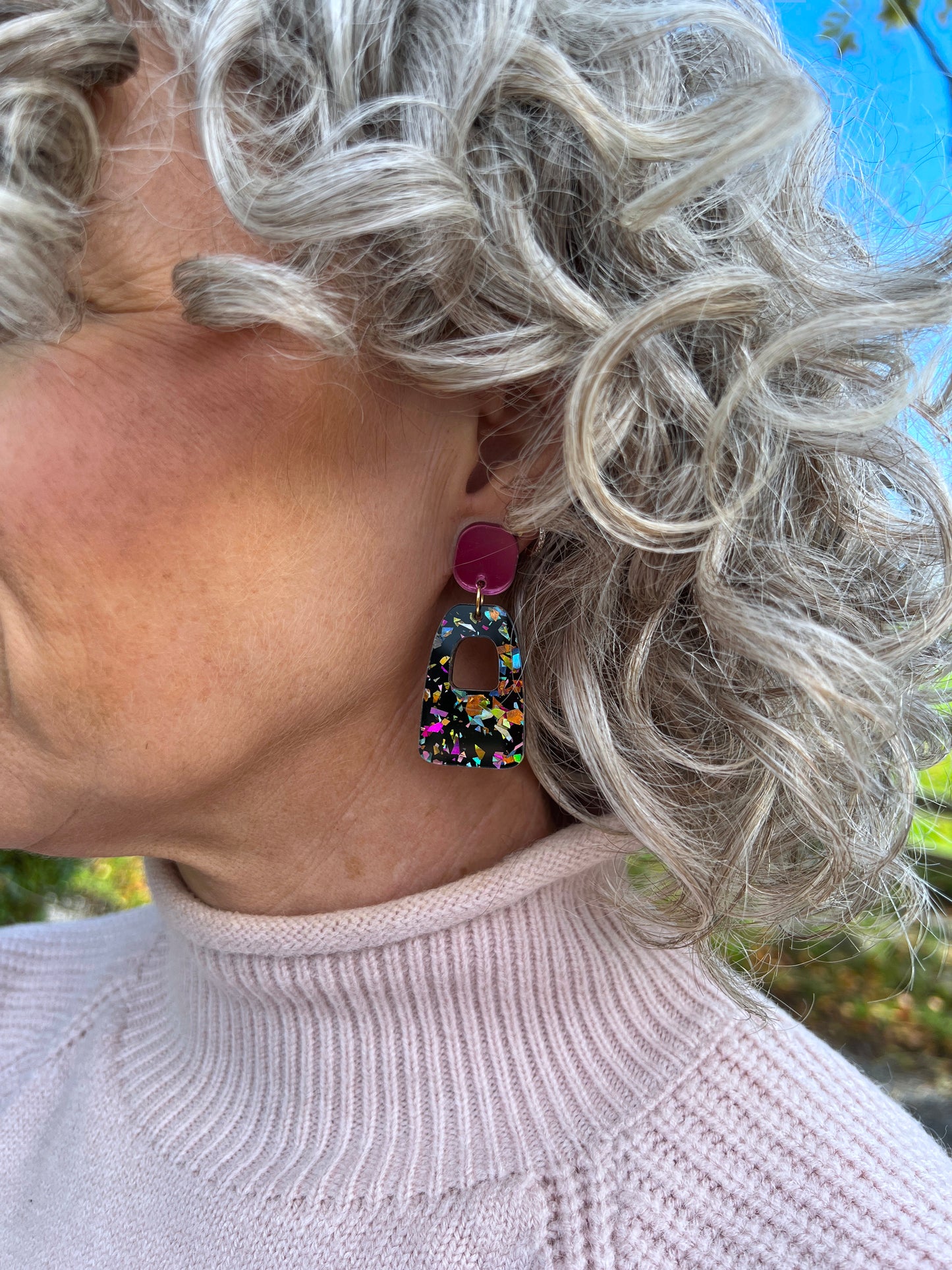 Person wearing colourful glitter earrings with a blurred background