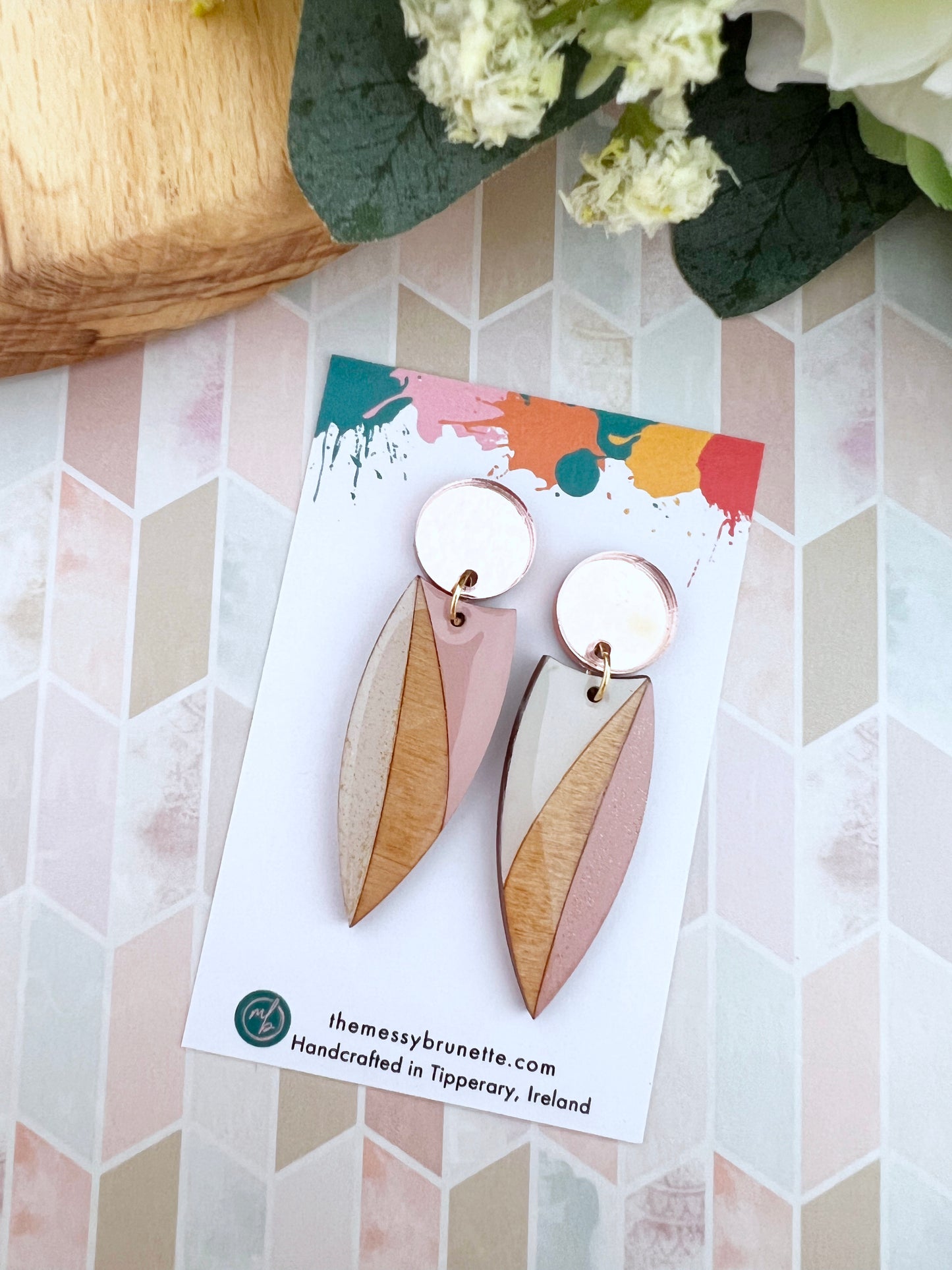 Pair of wood earrings in blush pink and sand on a colourful card with floral and wooden background