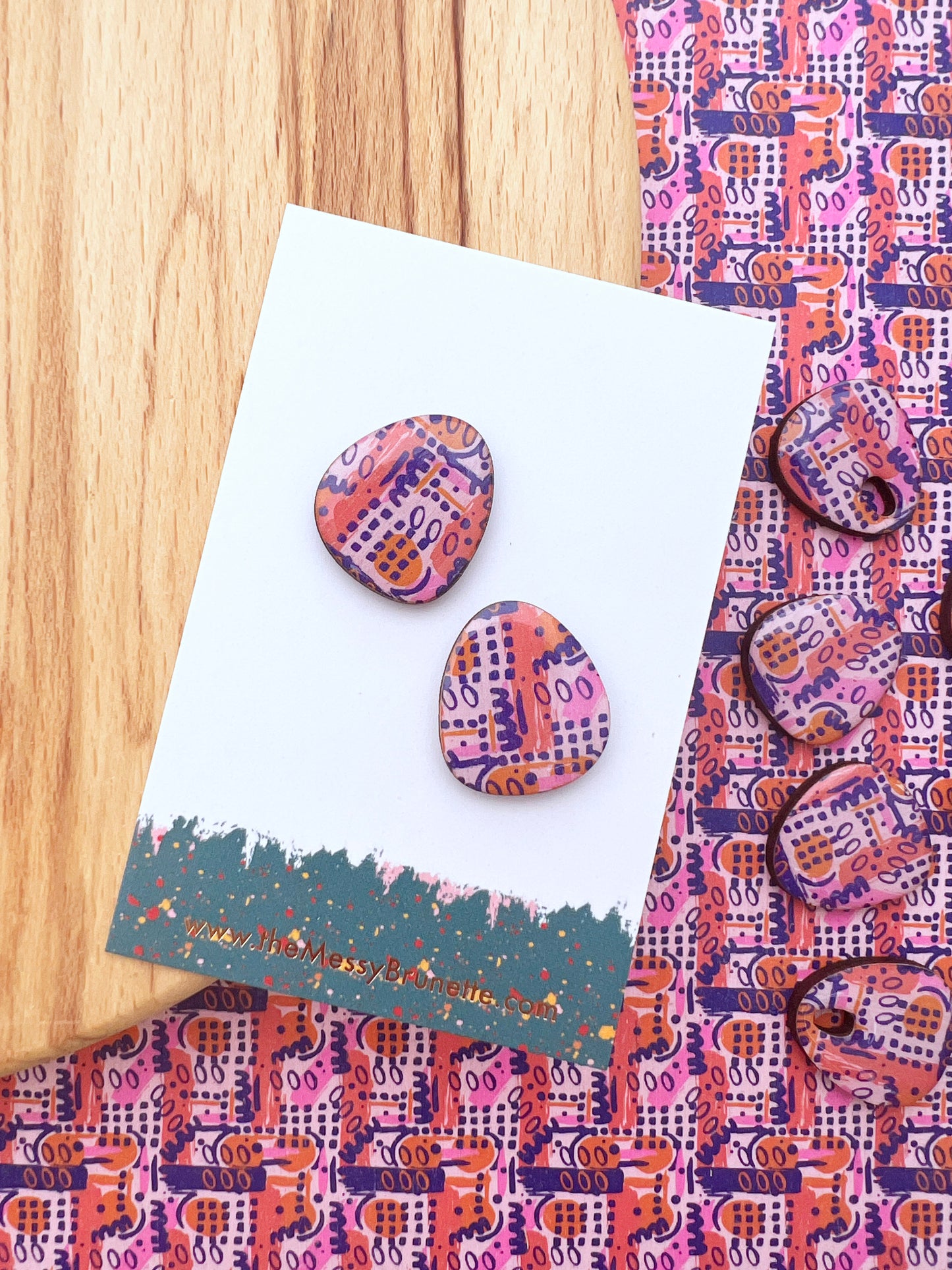 Colourful patterned earrings on a matching card with a wooden surface.