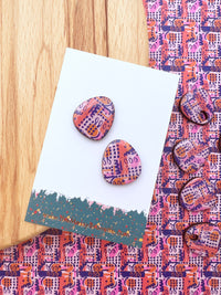 Colourful patterned earrings on a matching card with a wooden surface.