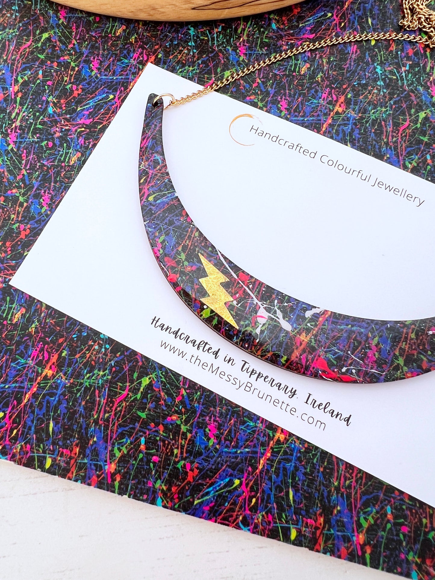 paint splatter wooden necklace with gold bolt layered to top on a painted background of messy brush strokes