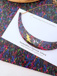 paint splatter wooden necklace with gold bolt layered to top on a painted background of messy brush strokes