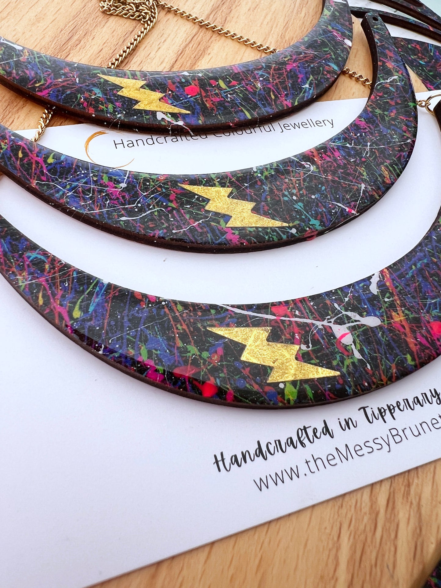 paint splatter wooden necklace with gold bolt layered to top on a painted background of messy brush strokes