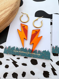 Orange lightning bolt earrings on a branded card with a polka dot background