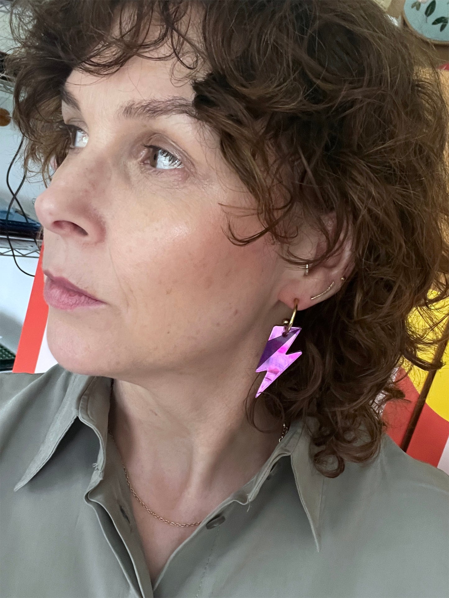 Close-up of a person with curly hair wearing bolt hoop earrings indoors.