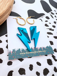 Turquoise lightning bolt earrings on a branded card with gold hoop earrings in the background.