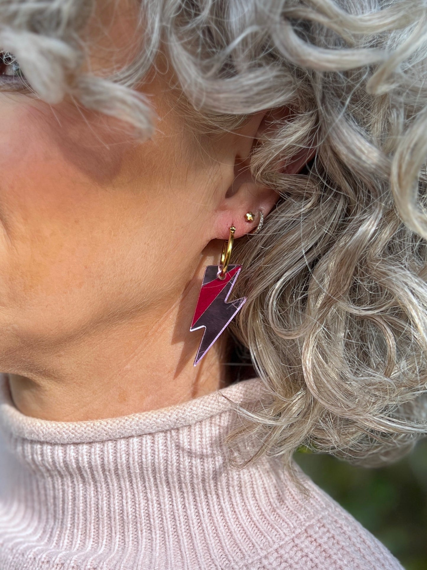 Close-up of a person wearing pink bolt hoop earrings 