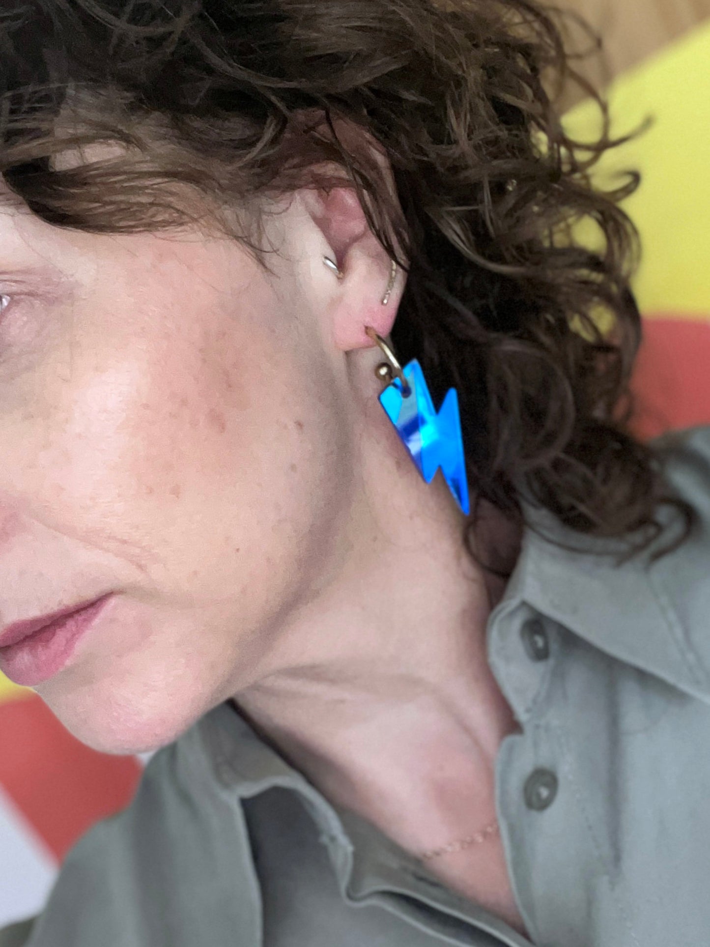 Close-up of a person wearing blue lightning bolt earrings with a blurred background.