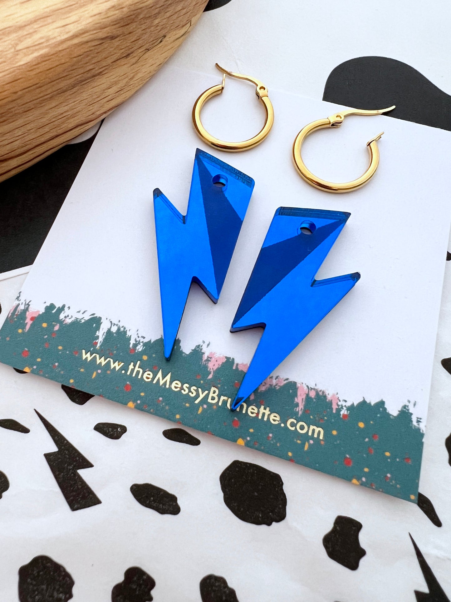 Blue lightning bolt earrings on a branded card with a black and white patterned surface.