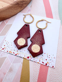 Burgundy red hoop earrings with gold accents on a patterned card
