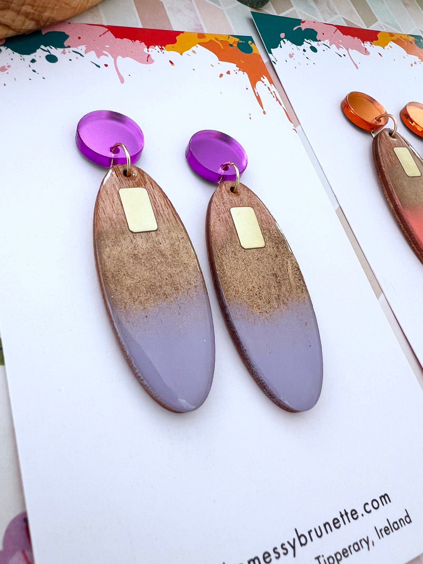 Pair of earrings with lavender and gold accents on a colourful background