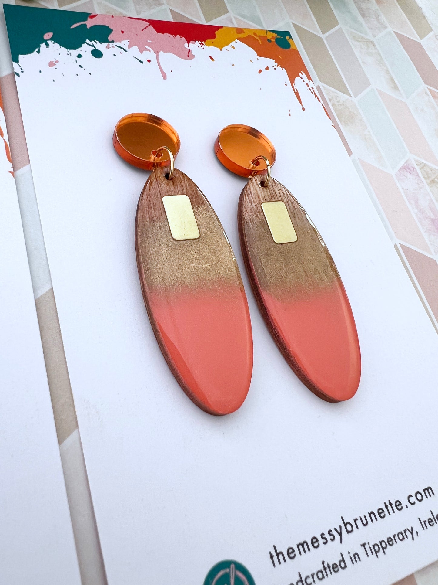 Pair of earrings with gold and coral design on a branded card.