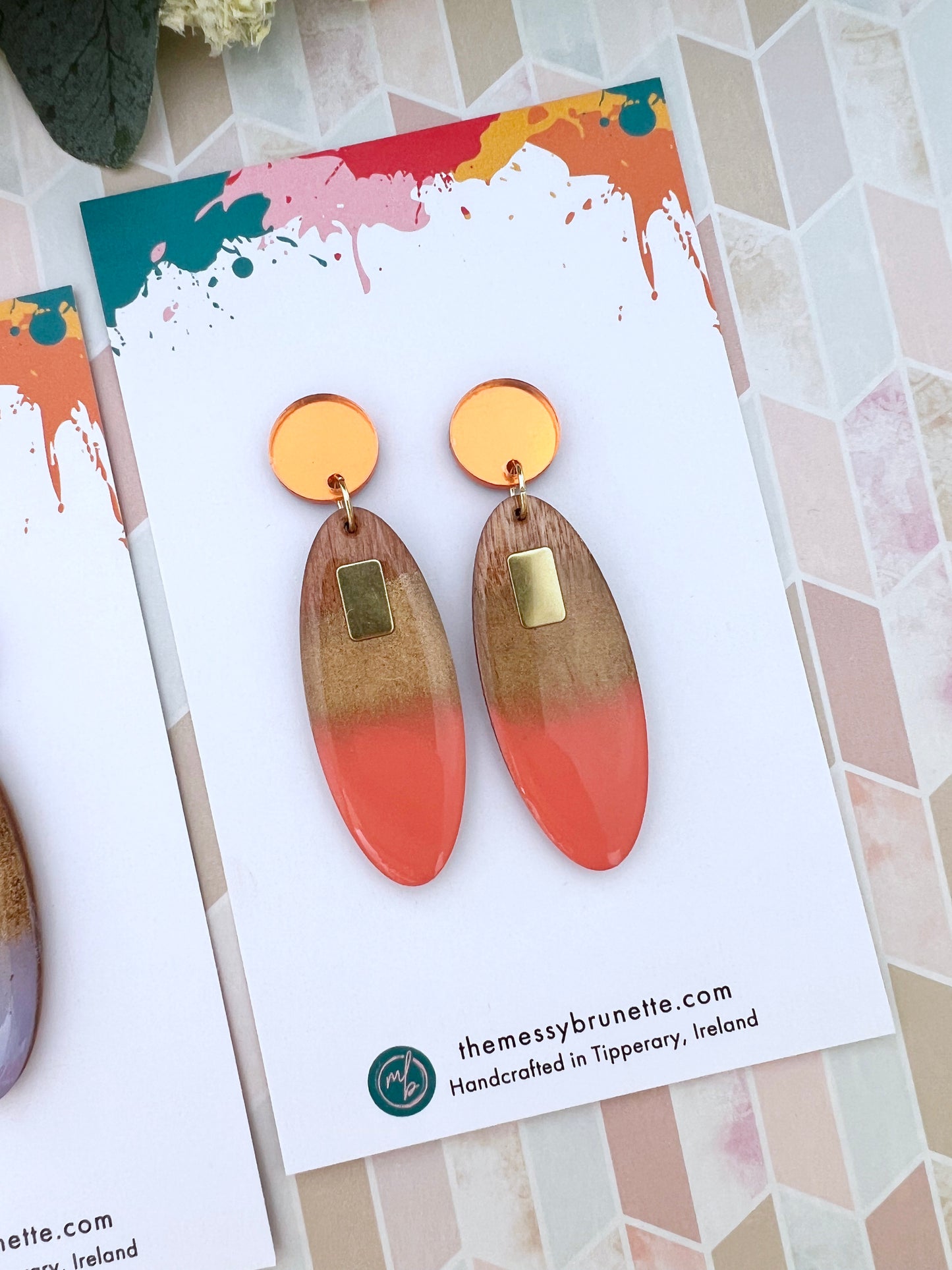 Pair of coral and gold oval type earrings on a colourful card with 'themessybrunette.com' branding.
