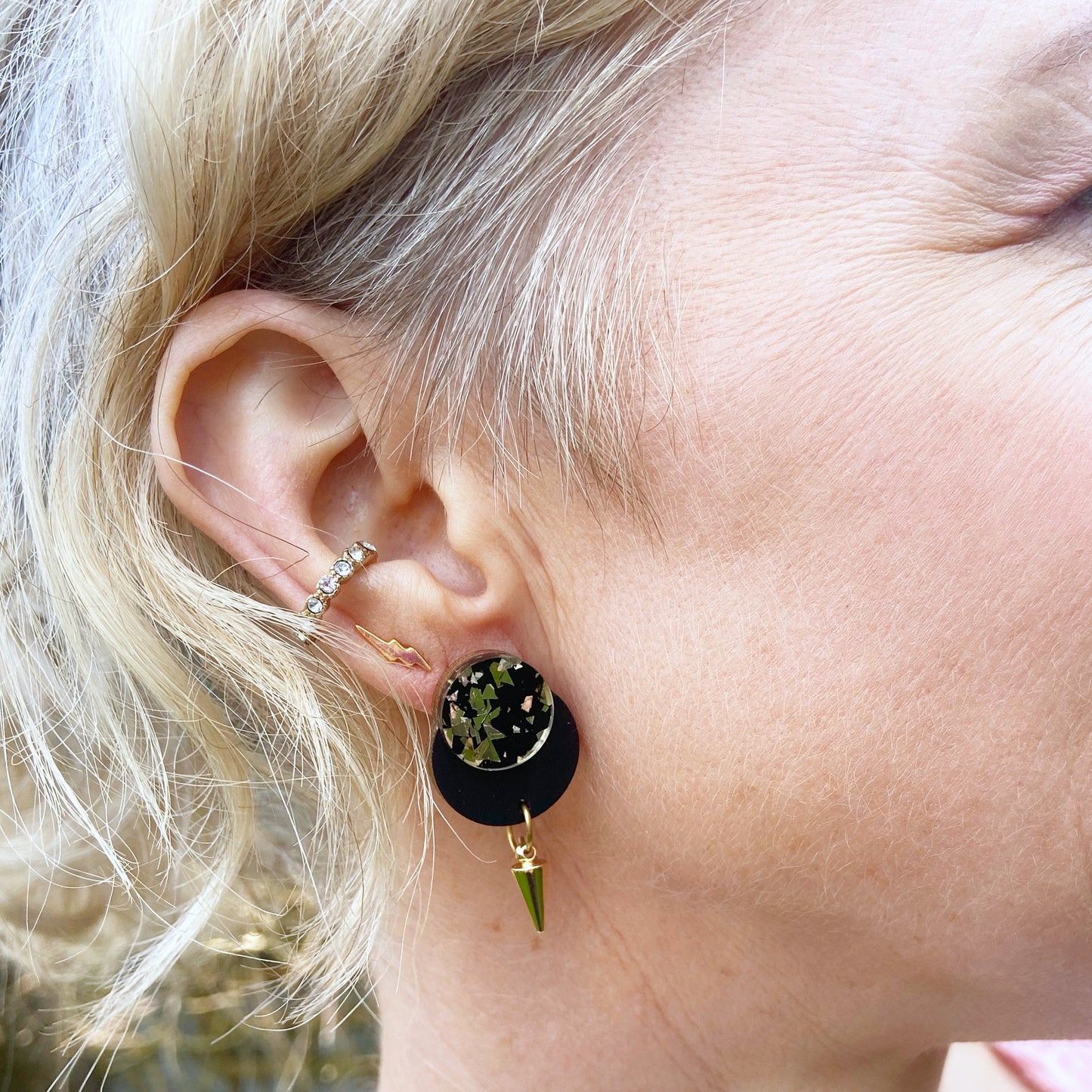 Close-up of an ear wearing black and gold glitter small dangle stud with spike