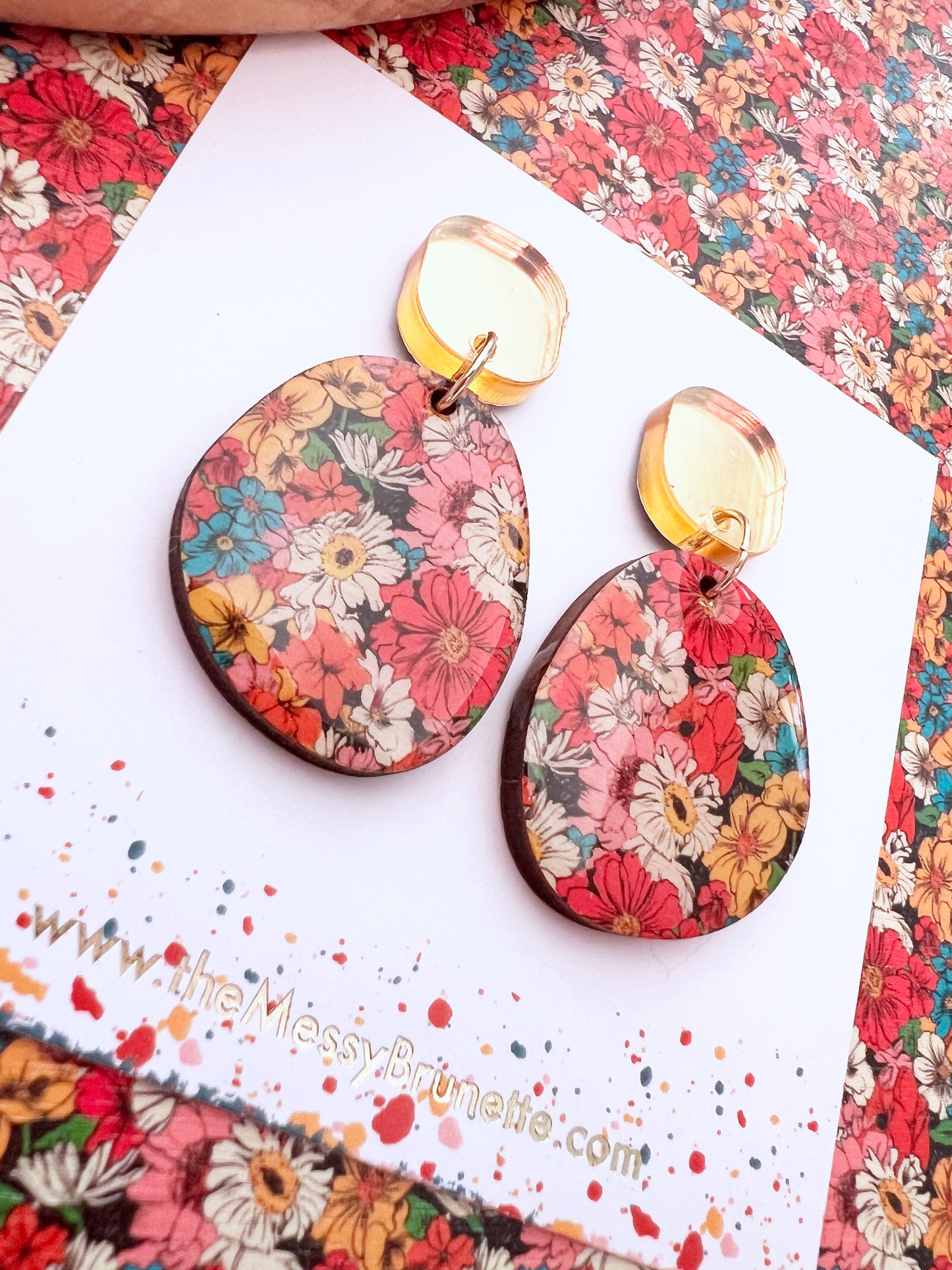 Floral patterned earrings on a colorful background with a website address.