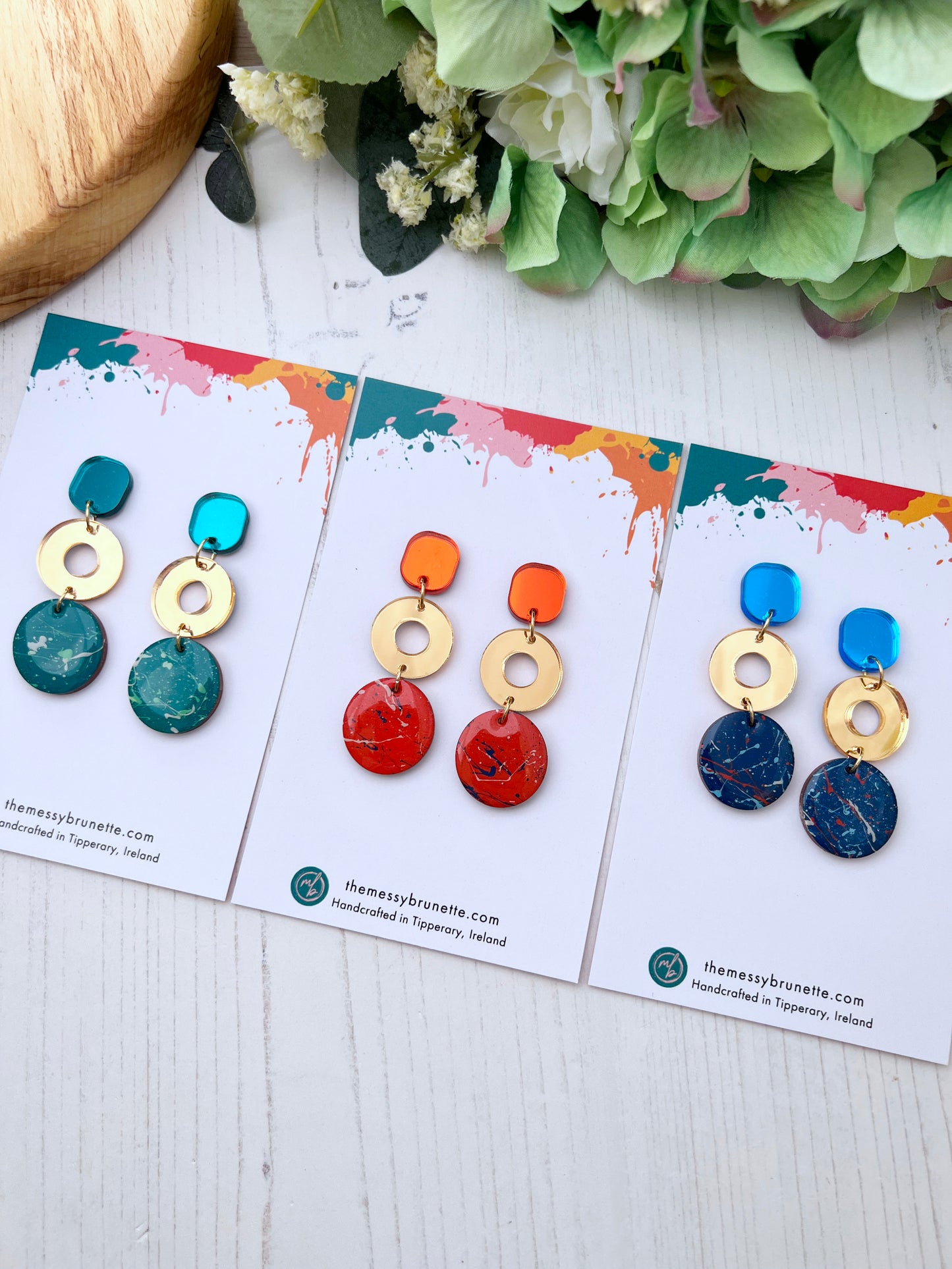 Colourful hand painted earrings on display cards with a decorative background