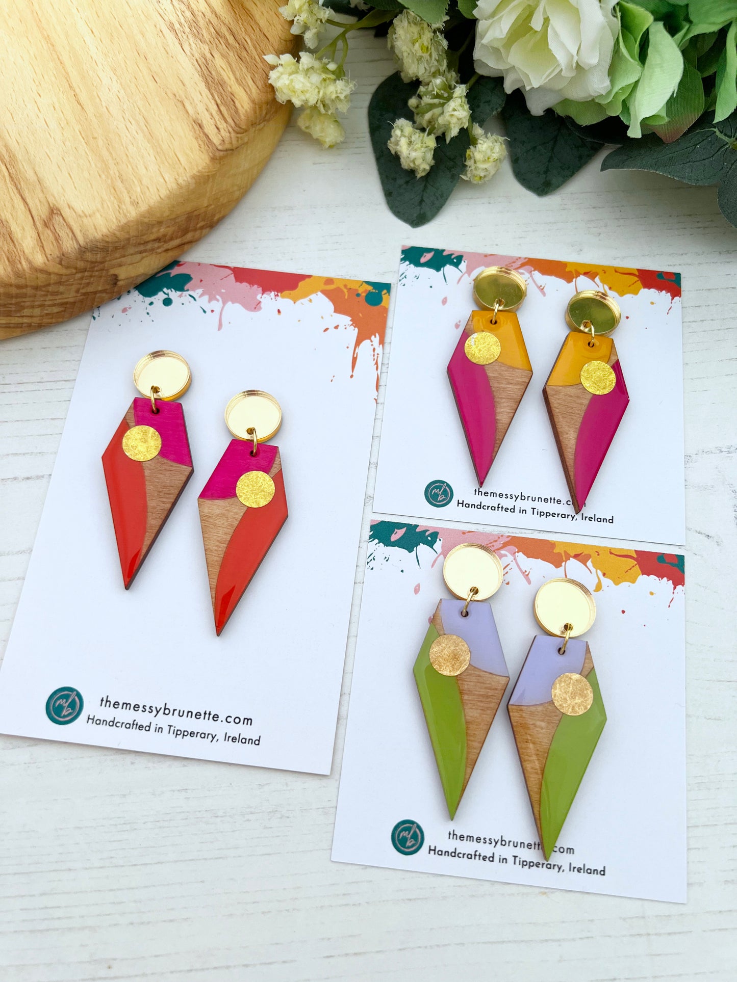 Colourful long geometric earrings on branded cards with flowers in the background