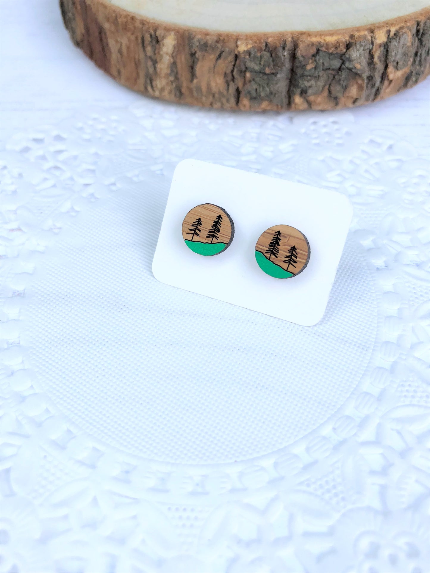 Wooden earrings with a trees etched onto surface and set against a white background