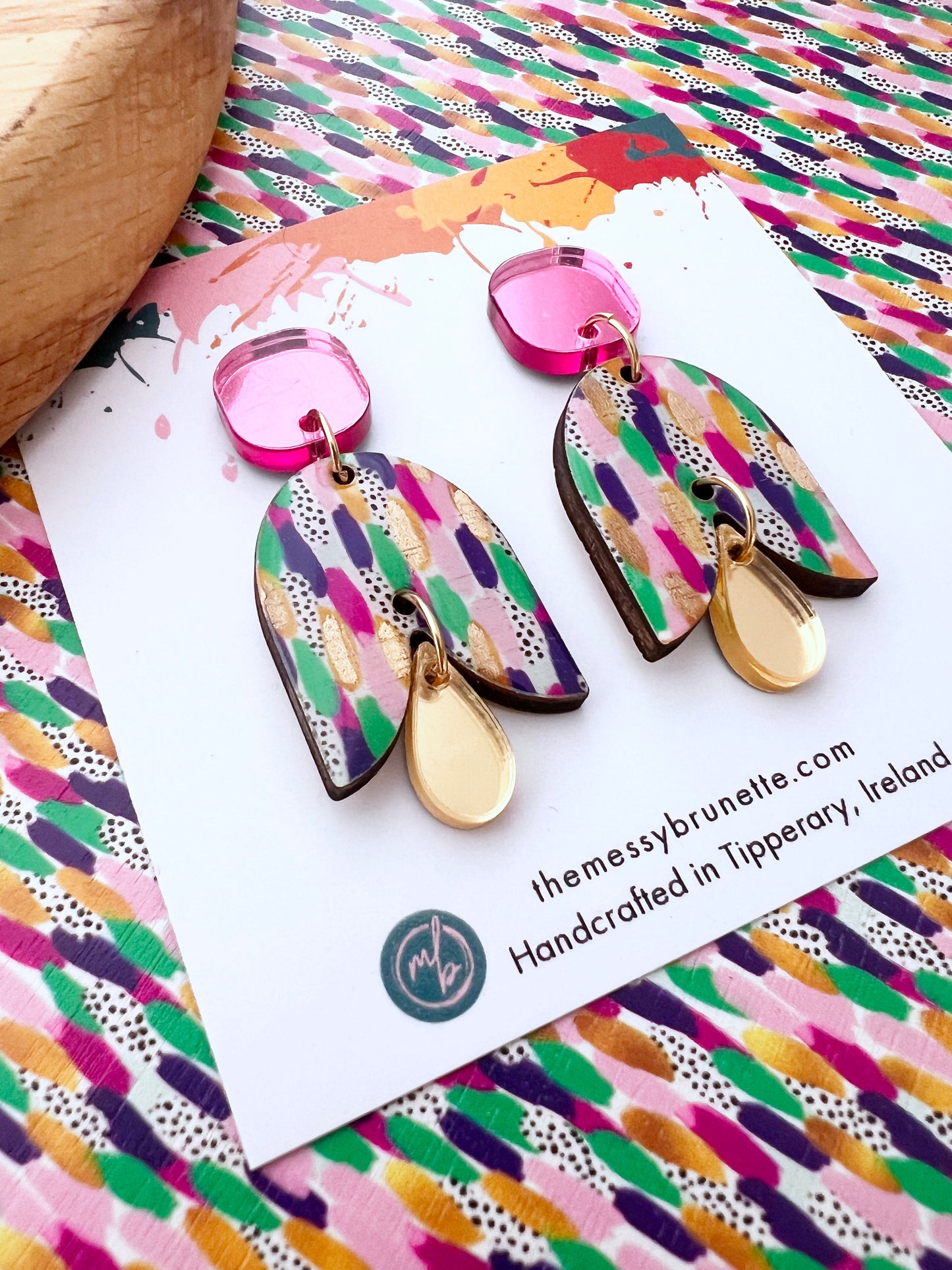 Painted wood earrings in a painted pattern effect with pink studs on a colourful  background