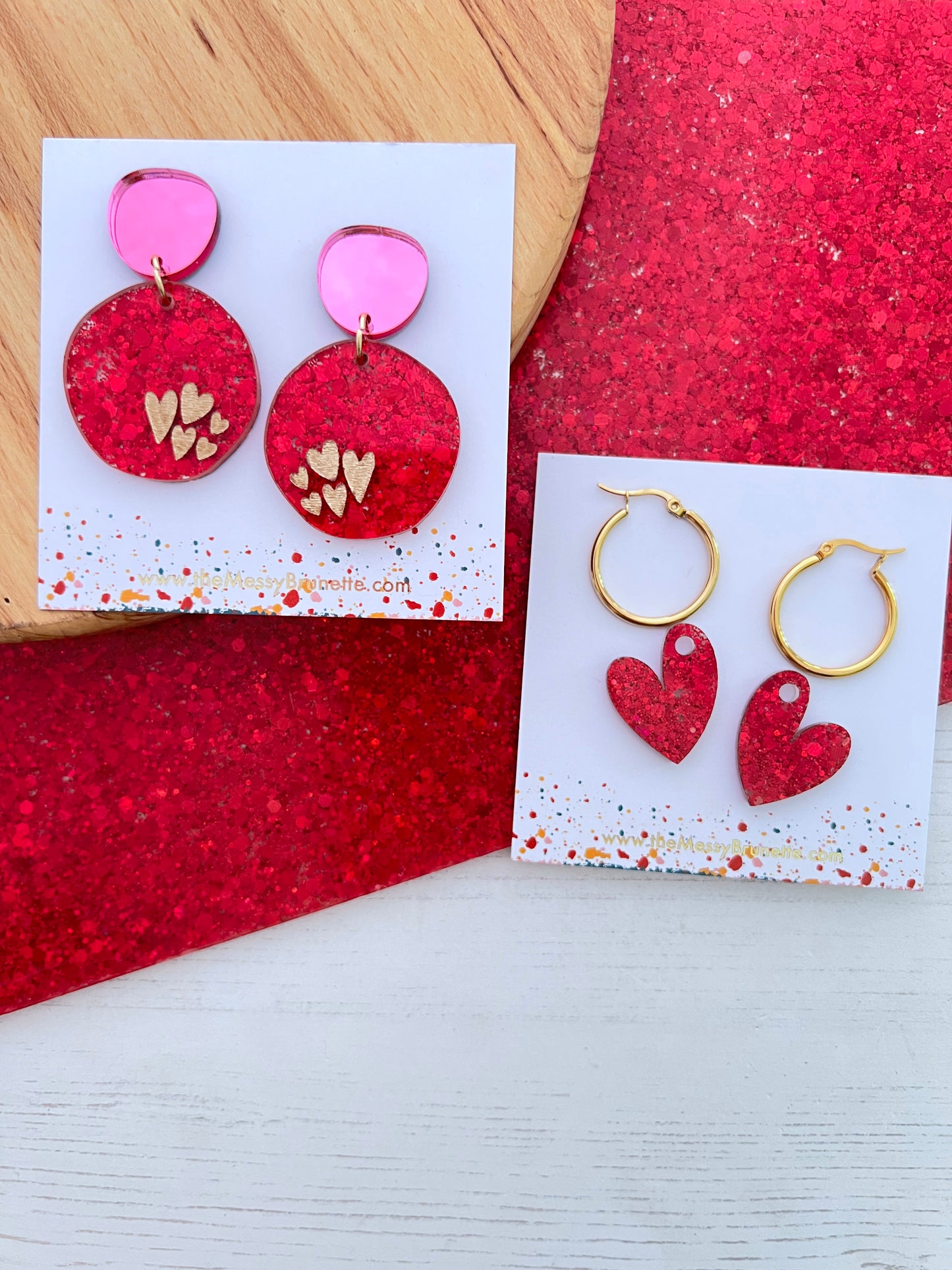 Red and pink heart-shaped earrings on a white card with a pink glittery background.
