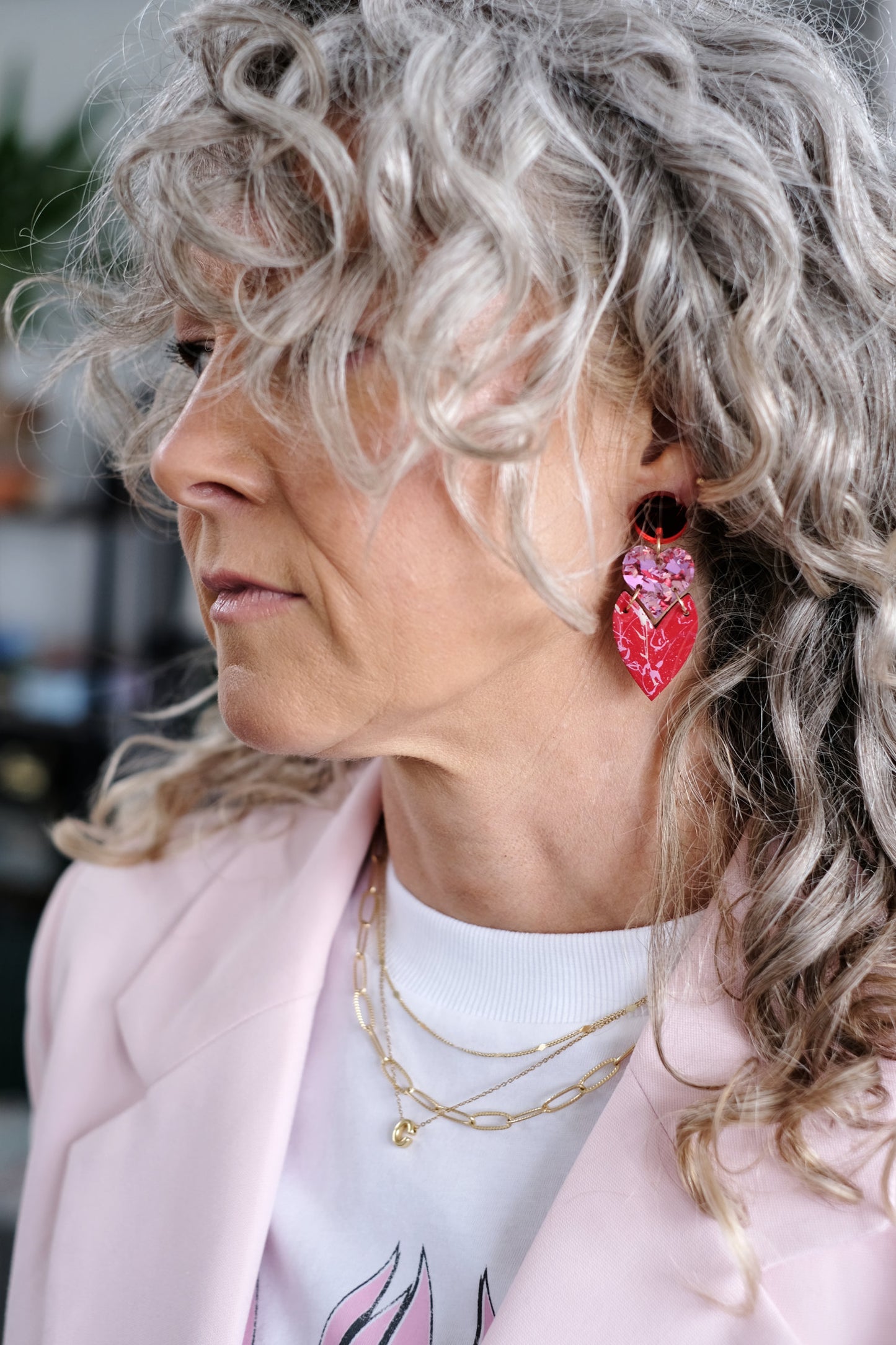 Woman with curly gray hair wearing pink heart-shaped earrings and a light pink jacket.