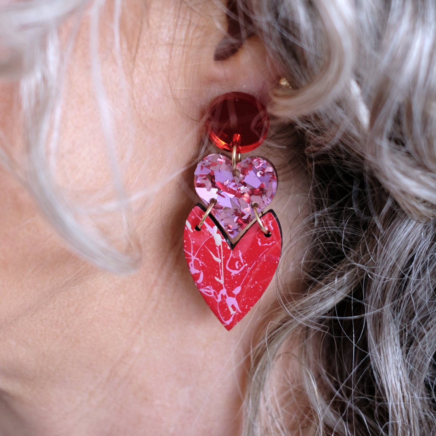 Close-up of a person wearing a red and pink heart-shaped earring.