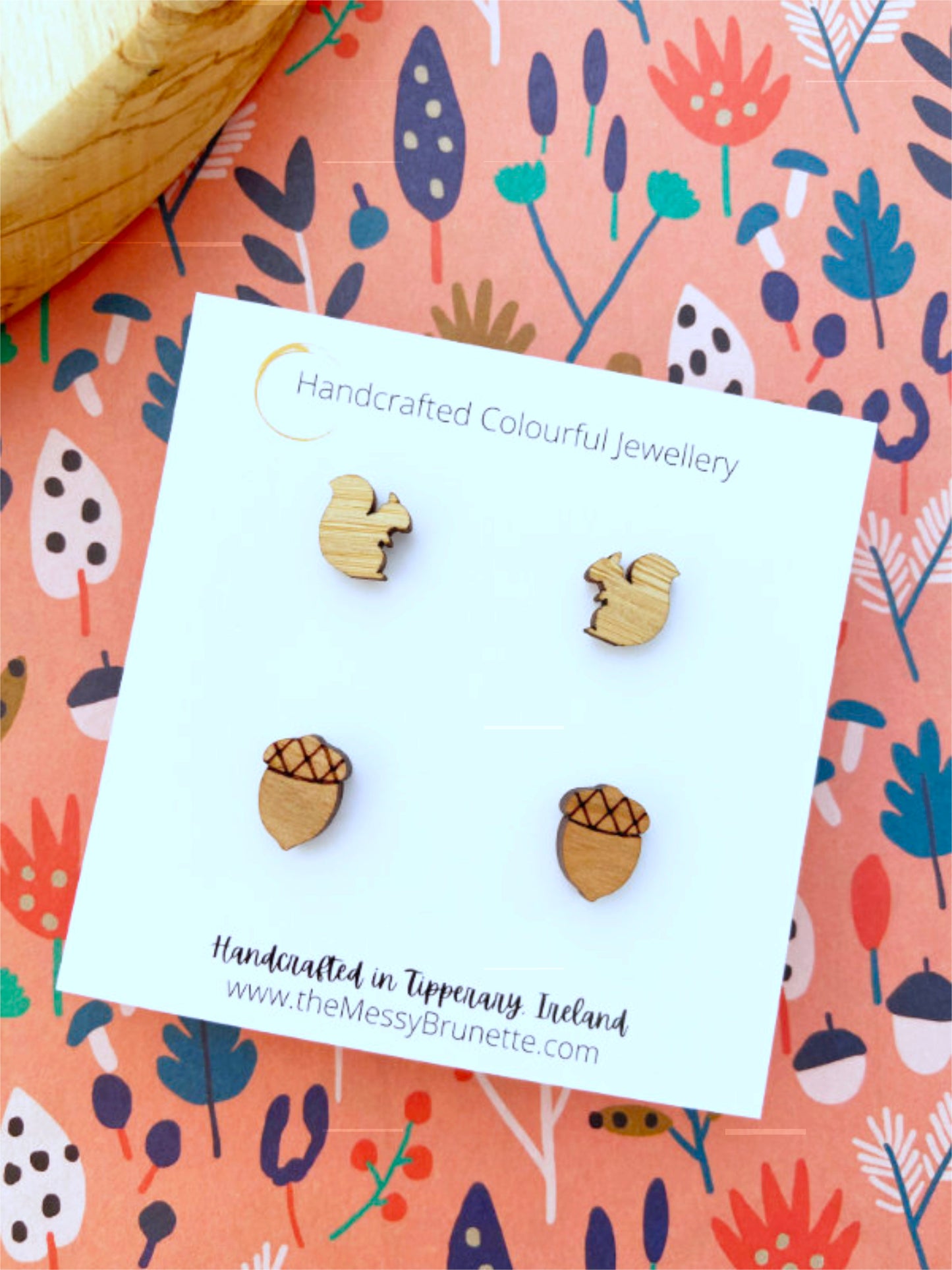 Wooden acorn and squirrel shaped earrings on a 'Handcrafted Colourful Jewellery' card with a floral patterned background.