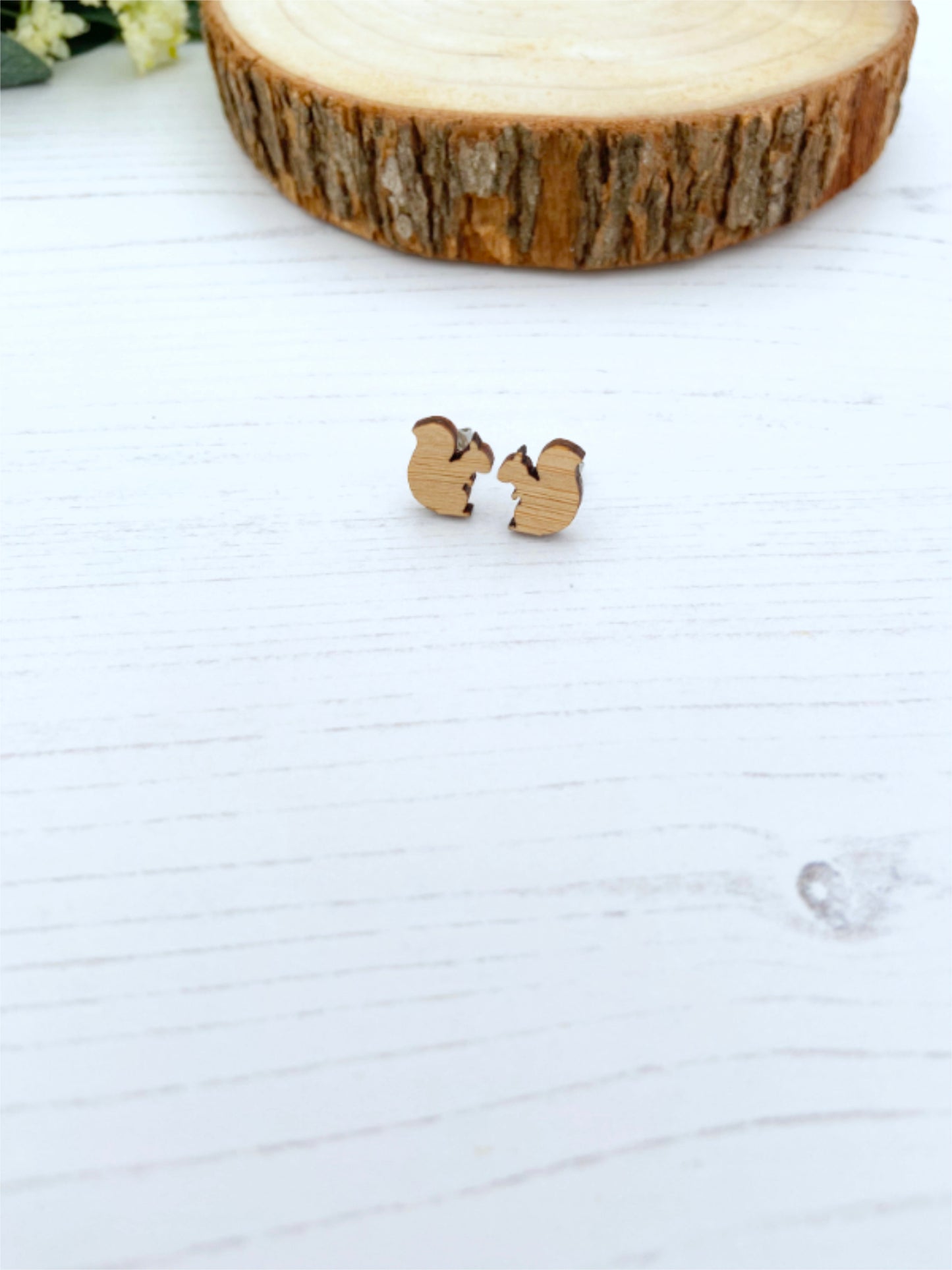 Wooden squirrel-shaped earrings on a white surface with a wooden block in the background.