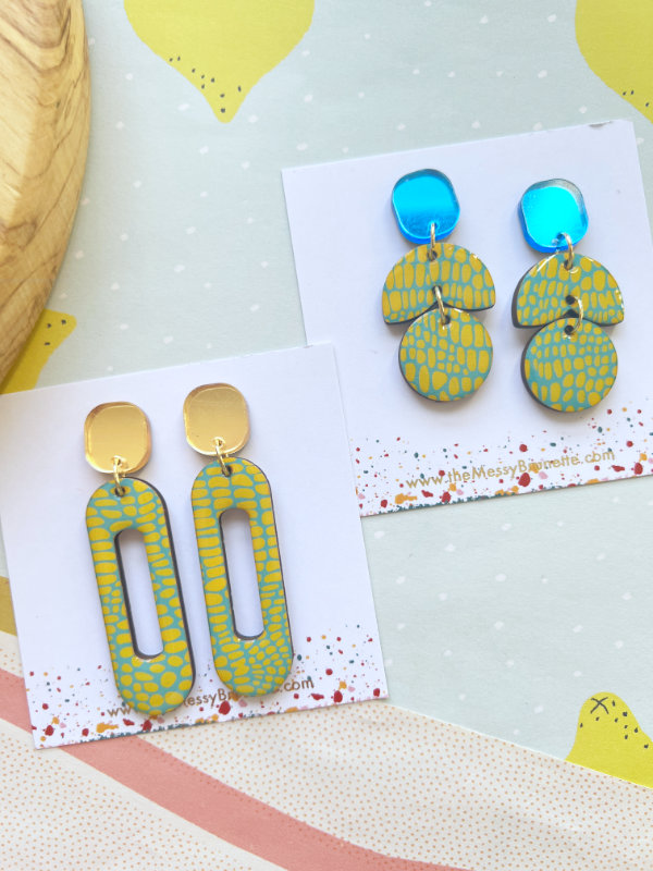 Pair of green and gold earrings on a branded card with a polka dot background