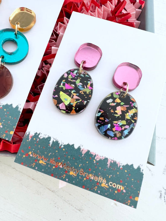 Colorful earrings on a branded card with a colorful background