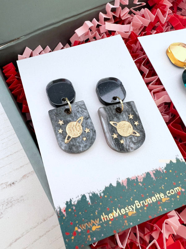 Marble-patterned earrings with gold planets on a 'the Messy Brunette' branded card.