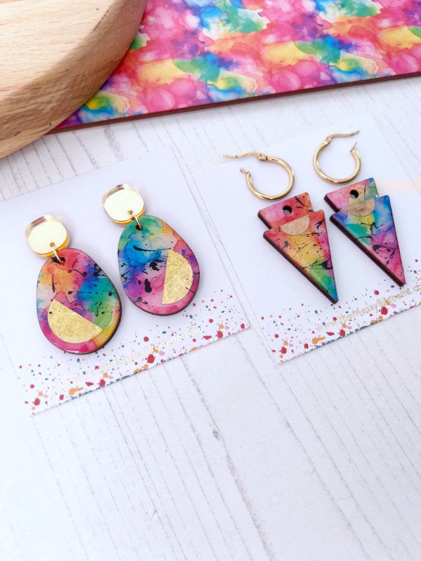 Colorful earrings on a white surface with a tie-dye background