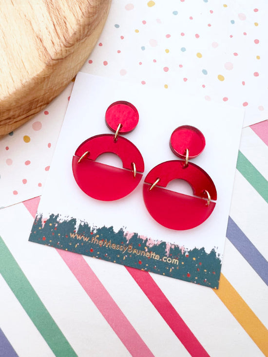 Red earrings on a colorful striped background with a brand label.