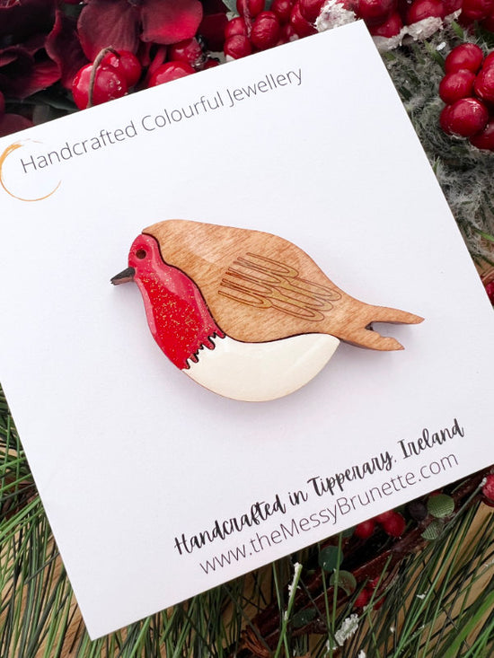 Wooden robin brooch on a white card with greenery and berries in the background